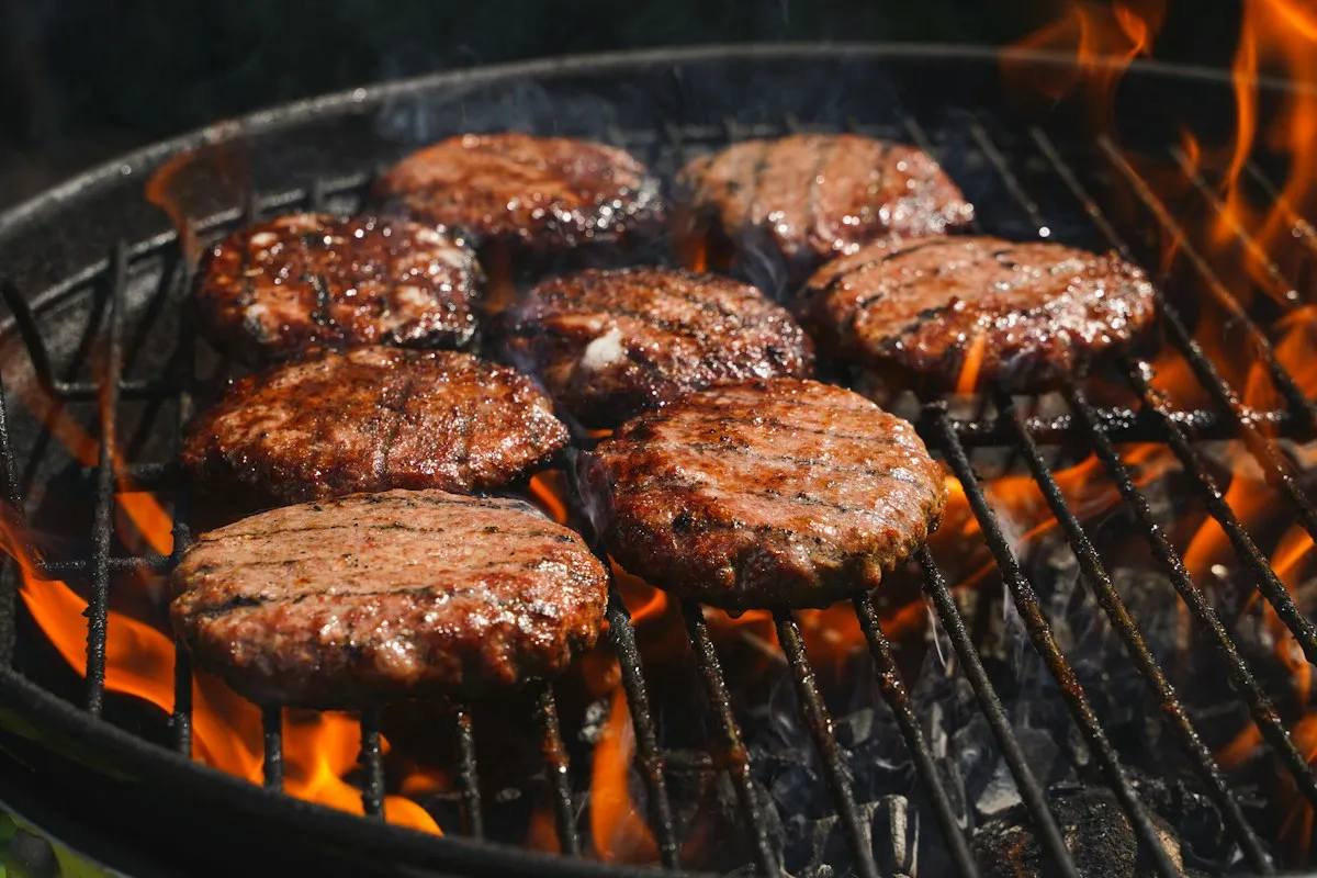 Beef burgers cooking on a barbecue grill over flames