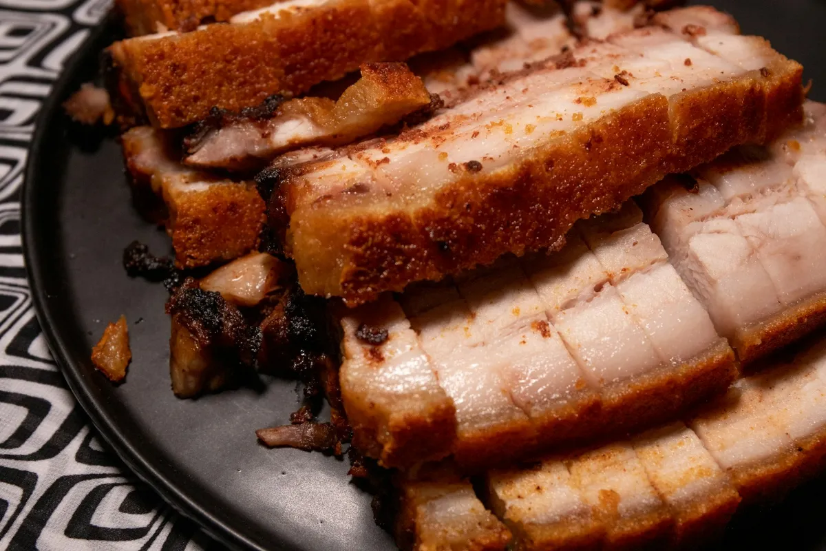 Slices of roast pork belly with thick crackling on a dark plate
